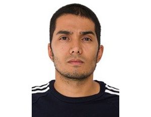 Persona con cabello corto, vestida con camiseta oscura que tiene franjas blancas en los hombros, frente a un fondo blanco.