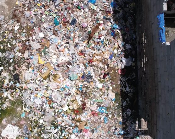 Gran acumulación de basura y desechos variados, incluyendo plásticos, papel y otros residuos, esparcidos sobre el suelo junto a una pared de concreto.