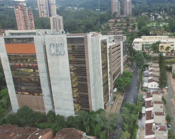 Vista aérea de un edificio con el logo “CES” en la fachada, rodeado de árboles, calles y construcciones residenciales, con edificios altos al fondo.