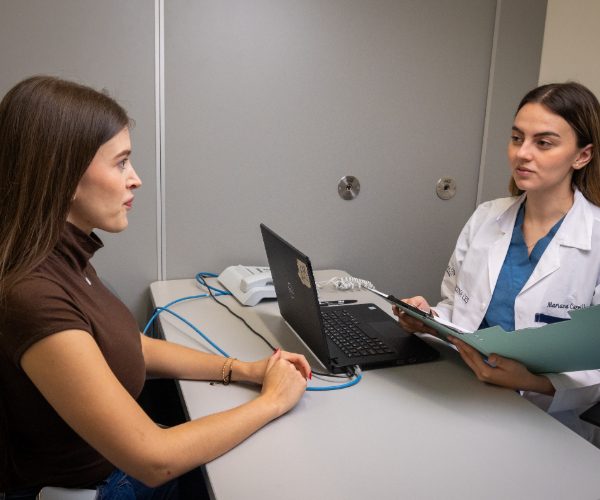 Dos personas sentadas frente a frente en una mesa, con un computador portátil y documentos sobre la superficie.