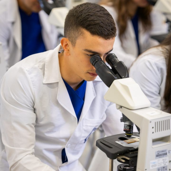 Persona con bata de laboratorio observando un microscopio en un entorno académico o científico