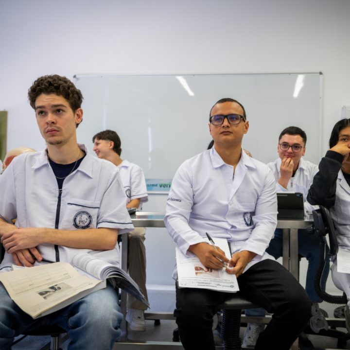 Grupo de personas con uniformes blancos sentadas en un aula, tomando notas y con materiales de estudio sobre las mesas.