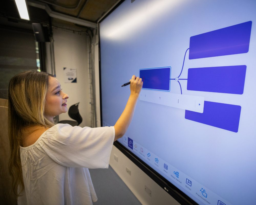 Persona interactúa con una pantalla táctil grande, conectando bloques rectangulares azules en un diagrama.