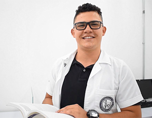 Persona con bata blanca y camiseta oscura sosteniendo un libro abierto en un entorno educativo.