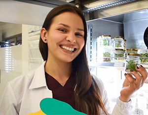 Persona con bata de laboratorio sosteniendo un frasco con plantas en un entorno de cultivo in vitro