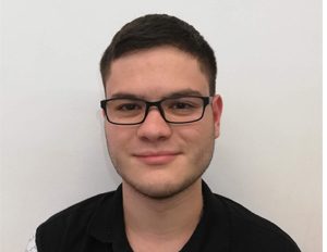 Persona con camiseta negra está frente a un fondo blanco liso, en una imagen tipo retrato.