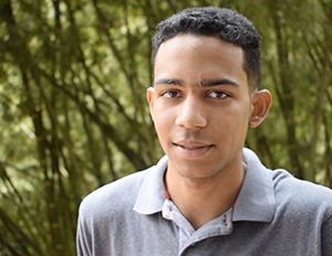 Persona con camiseta tipo polo gris está en un entorno natural con árboles y vegetación en el fondo.