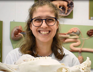 Una persona sostiene un cráneo animal en un entorno educativo, con modelos anatómicos de órganos expuestos en el fondo.