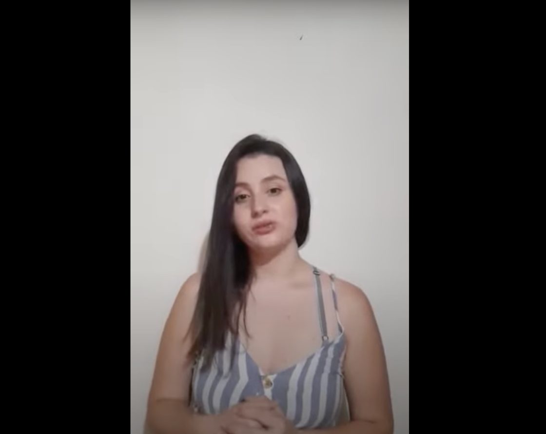 Persona de pie frente a una pared blanca, usando una blusa sin mangas con diseño de rayas verticales grises y blancas.