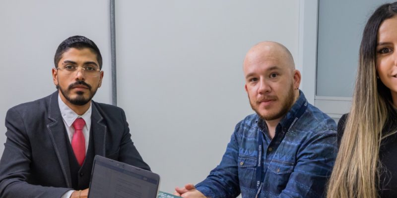 Varias personas sentadas alrededor de una mesa en una sala de reuniones, con documentos y un dispositivo electrónico sobre la mesa.