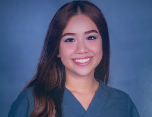 Persona con cabello largo y suelto viste uniforme clínico azul, posando frente a un fondo liso de color azul.