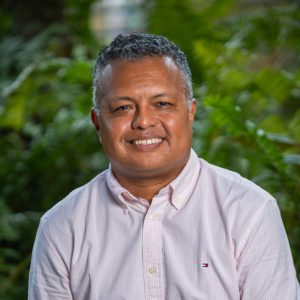 Persona de pie en un entorno exterior con vegetación, usando camisa de manga larga color rosa claro con botones y logotipo pequeño en el pecho.